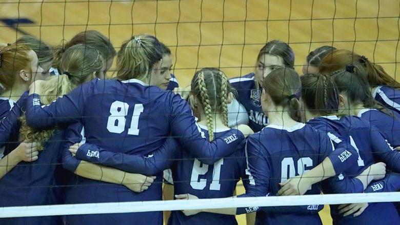 Penn State Altoona's 2023-24 women's volleyball team huddles before a game with a volleyball net in the foreground